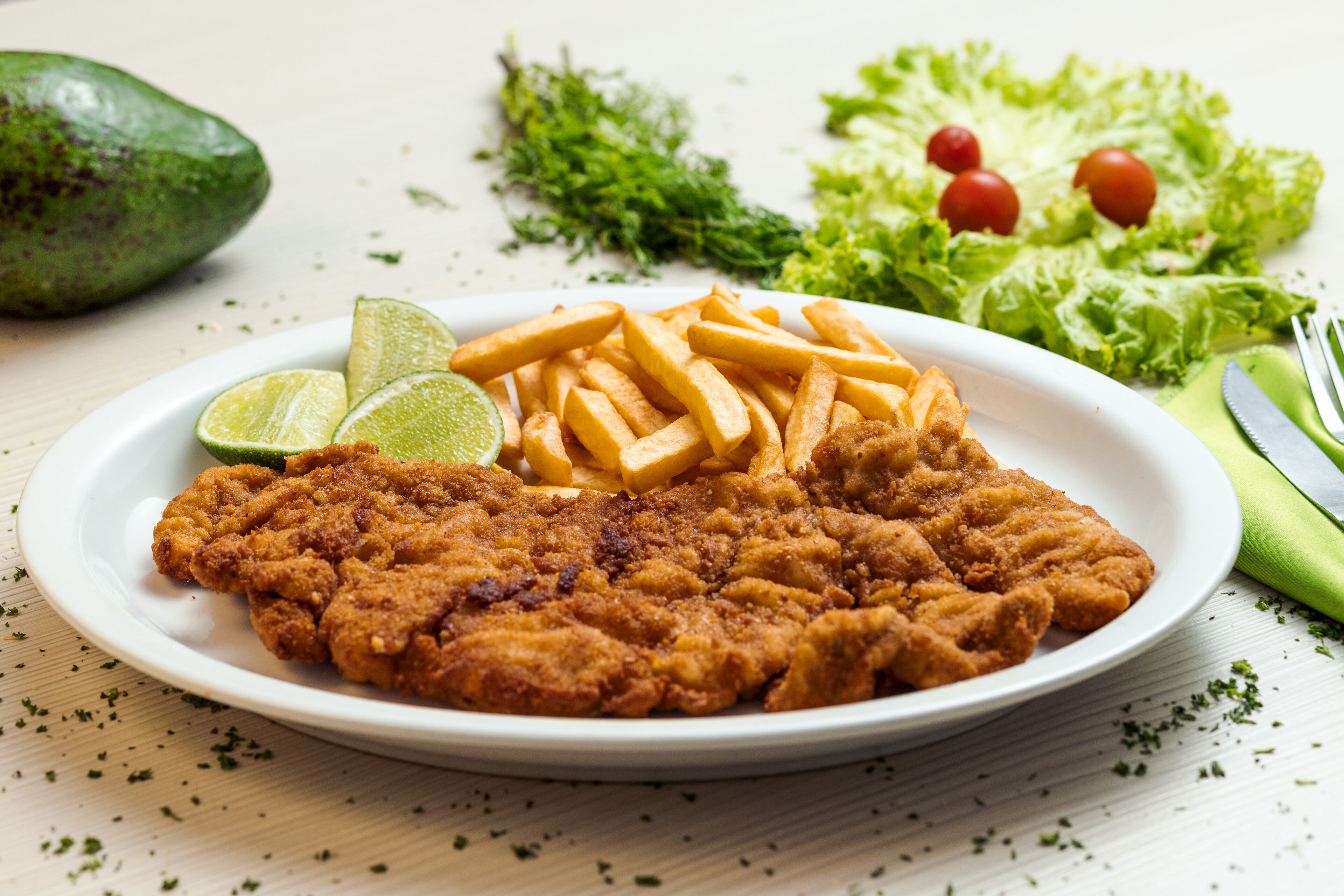 A plate with fried chicken, French fries, and lime wedges.