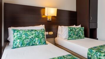 Habitación de hotel con dos camas, una mesita de noche, una lámpara de pared y un armario.