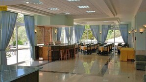 Un amplio vestíbulo de hotel con mostrador de recepción, varias mesas y sillas, y ventanas grandes con cortinas azules.