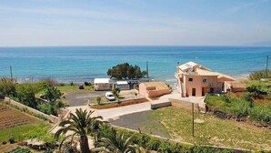 Una propiedad costera con una casa grande, un camino de acceso, coches aparcados y vista al mar.