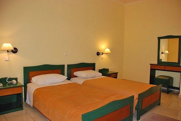 A double bed with green headboard and footboard, two bedside tables with lamps, and a mirror above a dresser.