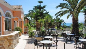 Un patio al aire libre con mesas y sillas, rodeado de palmeras y un edificio con arcos.