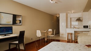 Una habitación de hotel con cama, escritorio con computadora, silla, mesa de comedor y kitchenette.