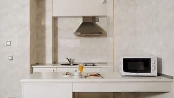 Una cucina moderna con mobili bianchi, lavello in acciaio inossidabile, microonde integrato e un piccolo spazio pranzo con tavolo e sedie.