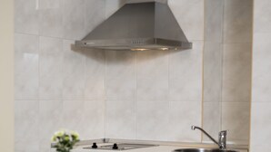 Una cocina moderna con una campana extractora de acero inoxidable, una encimera blanca y un comedor con una mesa dispuesta para el desayuno.