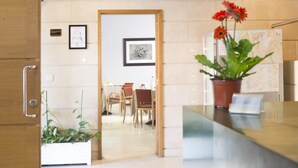 Un área de recepción con un mostrador de madera, una planta en maceta con flores rojas y un cuadro en la pared.