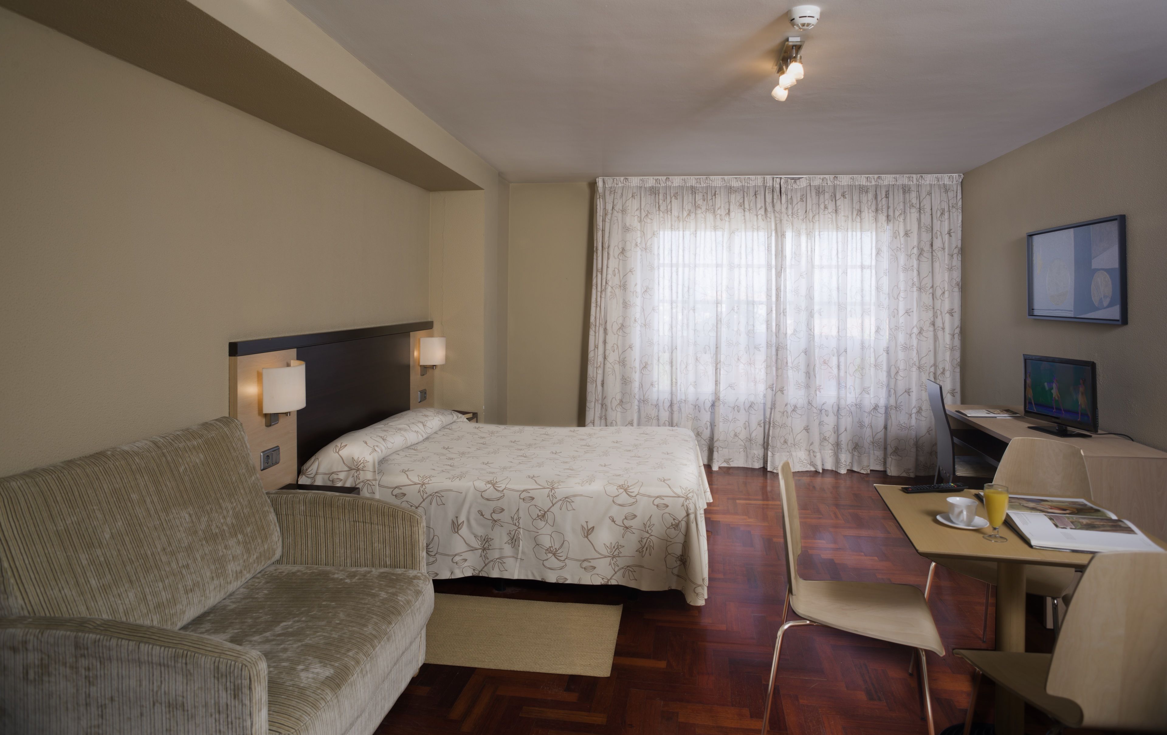 A hotel room with a bed, a sofa, a desk with a computer, a chair, and a television.
