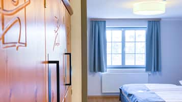 A bedroom with a bed, a window with curtains, a radiator, and a wooden wardrobe with a mirror.