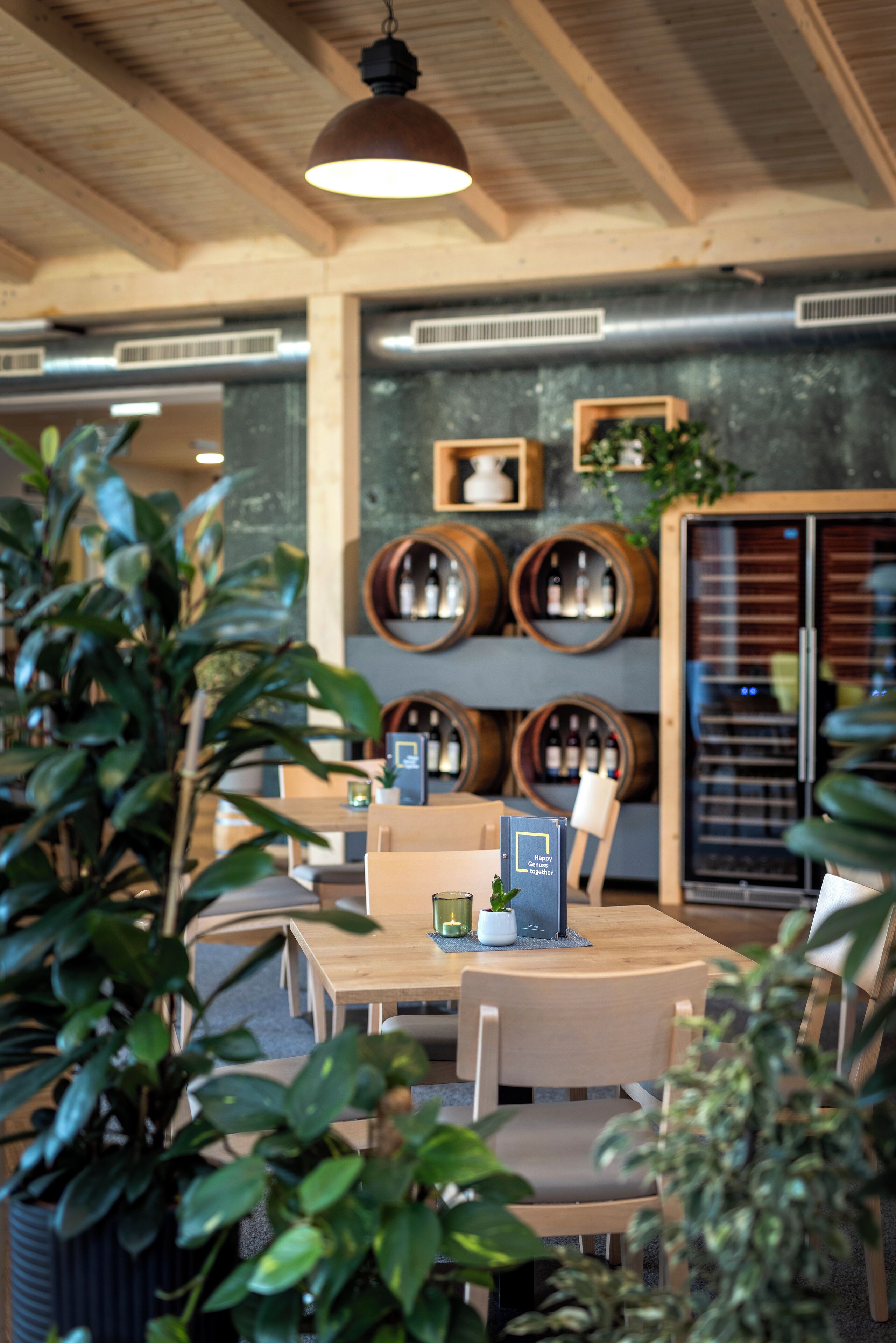 Un restaurant avec des tables et des chaises en bois, des plantes en pot et des tonneaux à vin accrochés au mur.