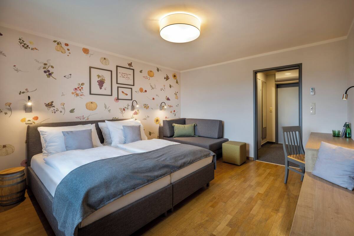 Un dormitorio con una cama grande, un sofá, una silla y una mesita. Hay decoraciones en la pared y una lámpara en el techo.