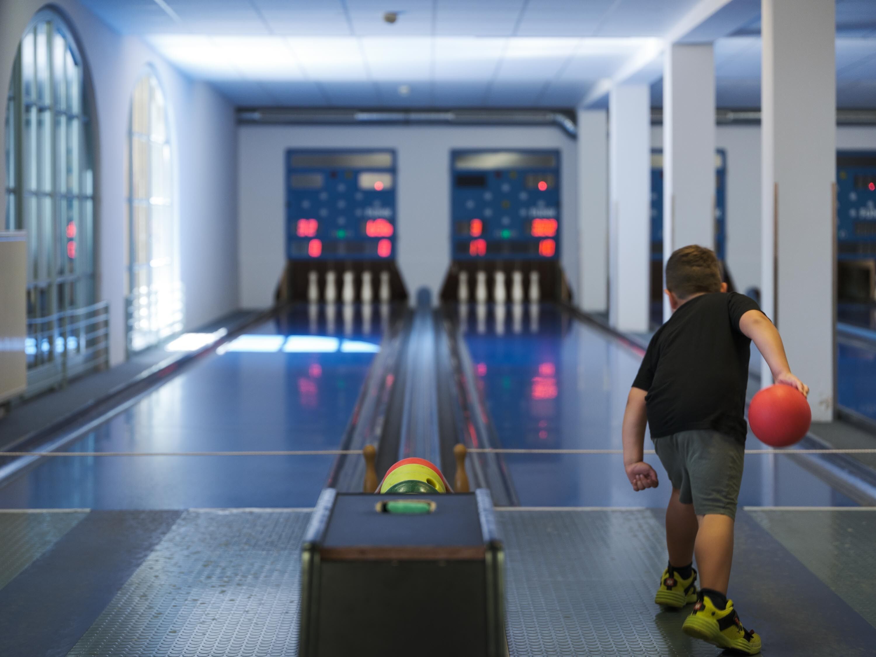 A bowling alley with a child holding a bowling ball, approaching the lane.