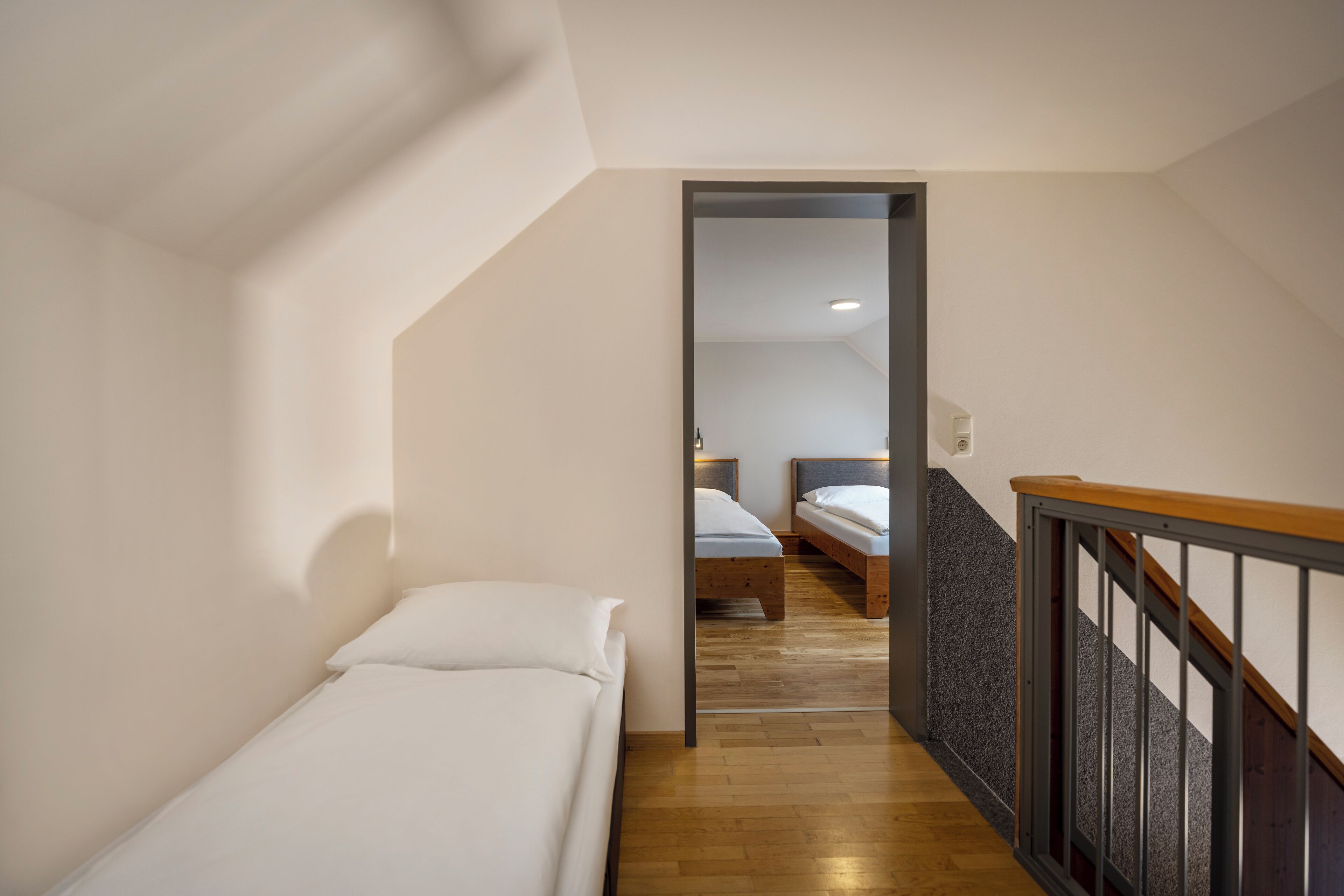 Un estrecho pasillo con piso de madera que conduce a un dormitorio con cama y mesita de noche.