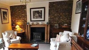 Una sala de estar acogedora con chimenea, pared de piedra y muebles blancos.