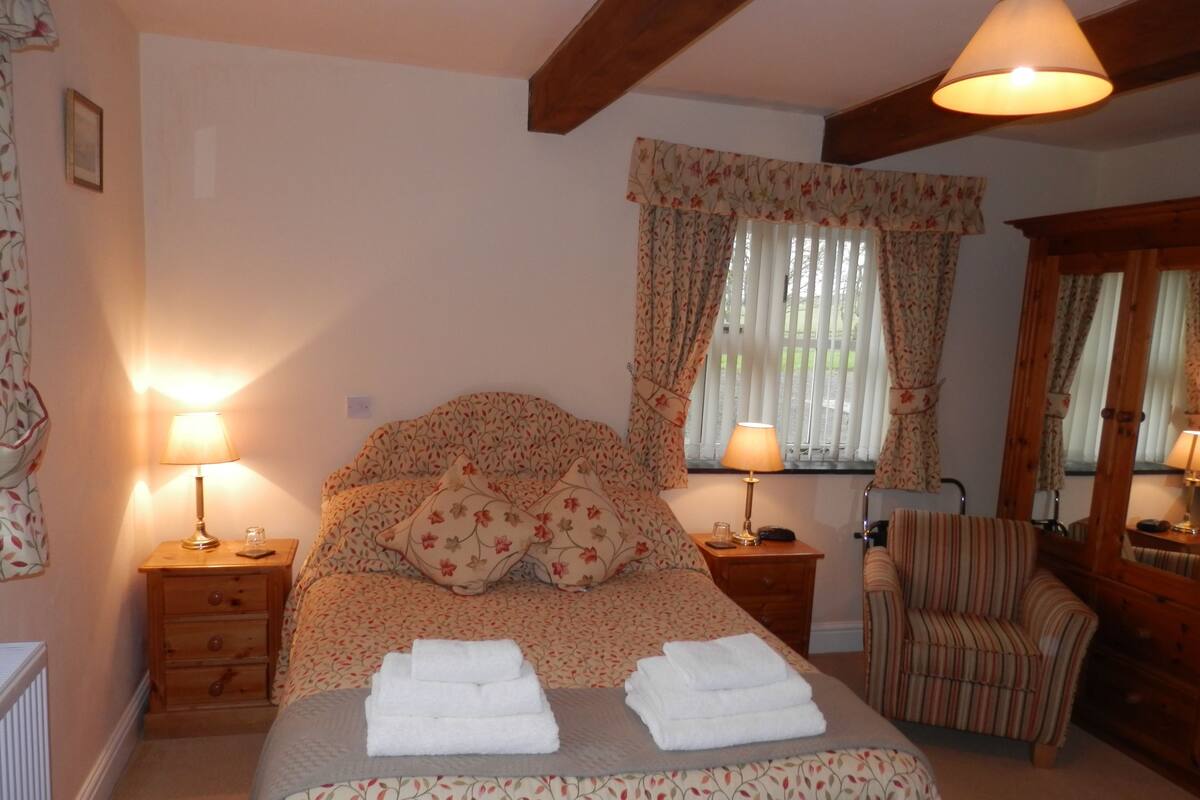 Une chambre à coucher avec un lit, deux tables de chevet, une chaise et une fenêtre avec des rideaux.