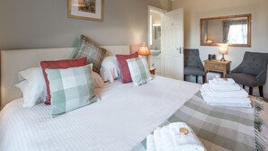 Habitación de hotel con una cama grande, dos mesitas de noche, una silla, un espejo y una puerta que da a un baño.