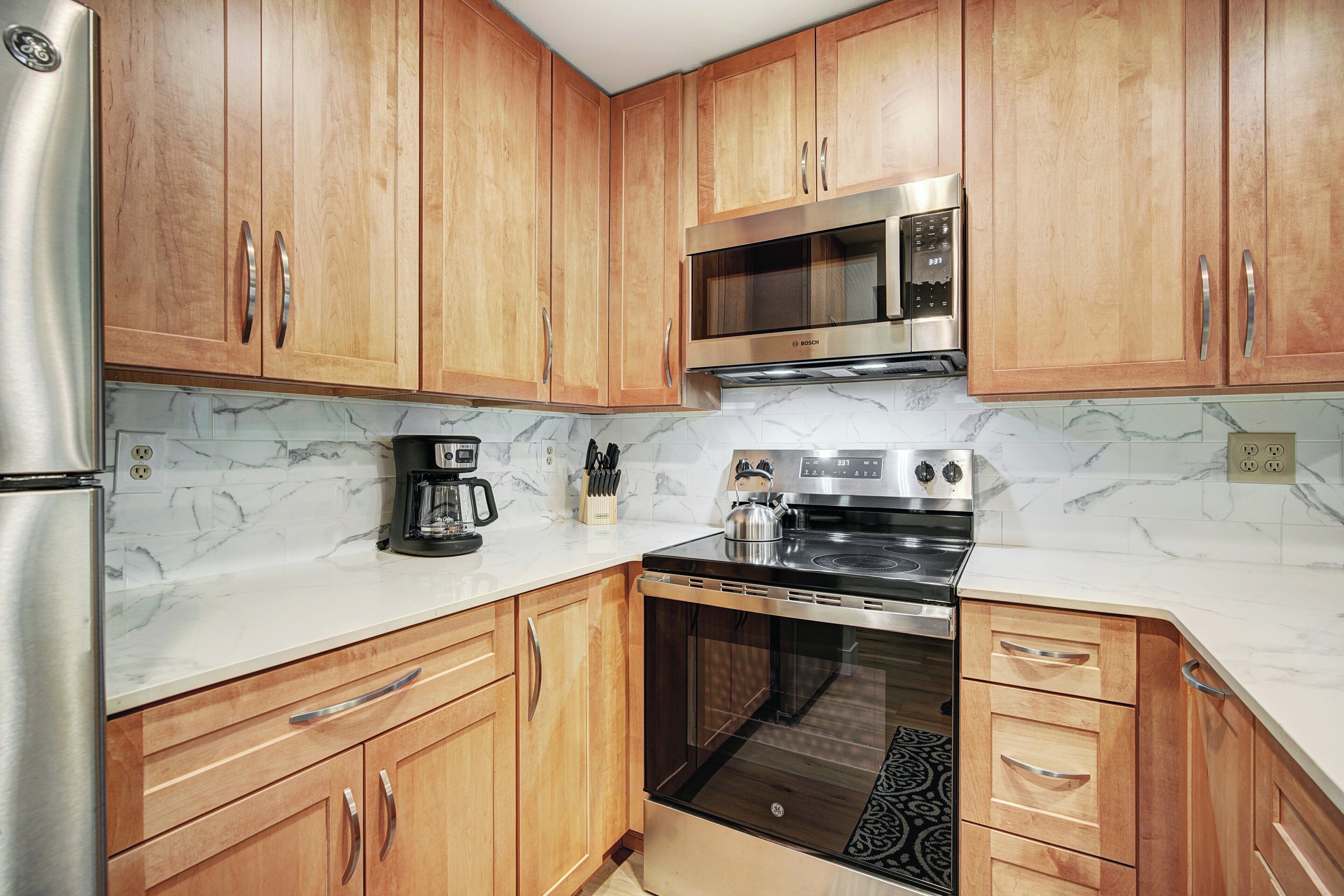 A kitchen with wooden cabinets, a stainless steel refrigerator, a Bosch microwave, a Bosch coffee maker, and a Bosch oven.