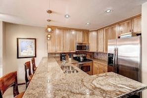 A kitchen with wooden cabinets, a granite countertop, stainless steel appliances, and pendant lighting.