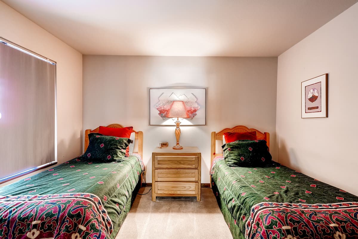 Un dormitorio con dos camas individuales, una mesita de noche con lámpara y un cuadro enmarcado en la pared.