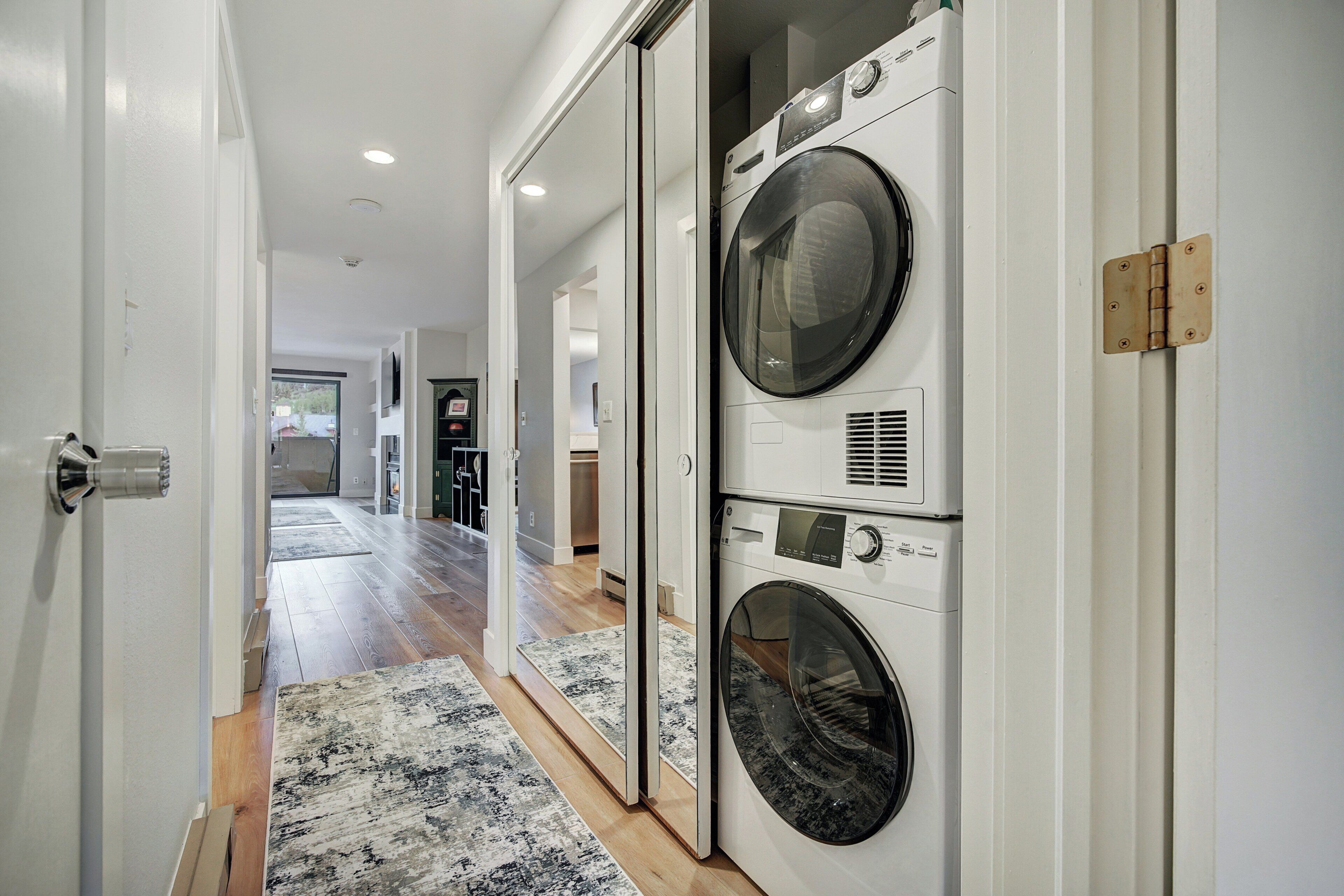 A laundry room with stacked washers and dryers, a wooden floor, and a hallway leading to other rooms.