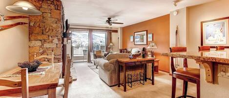 A cozy living room with a stone wall, a dining area with wooden furniture, and a kitchen with a granite countertop.