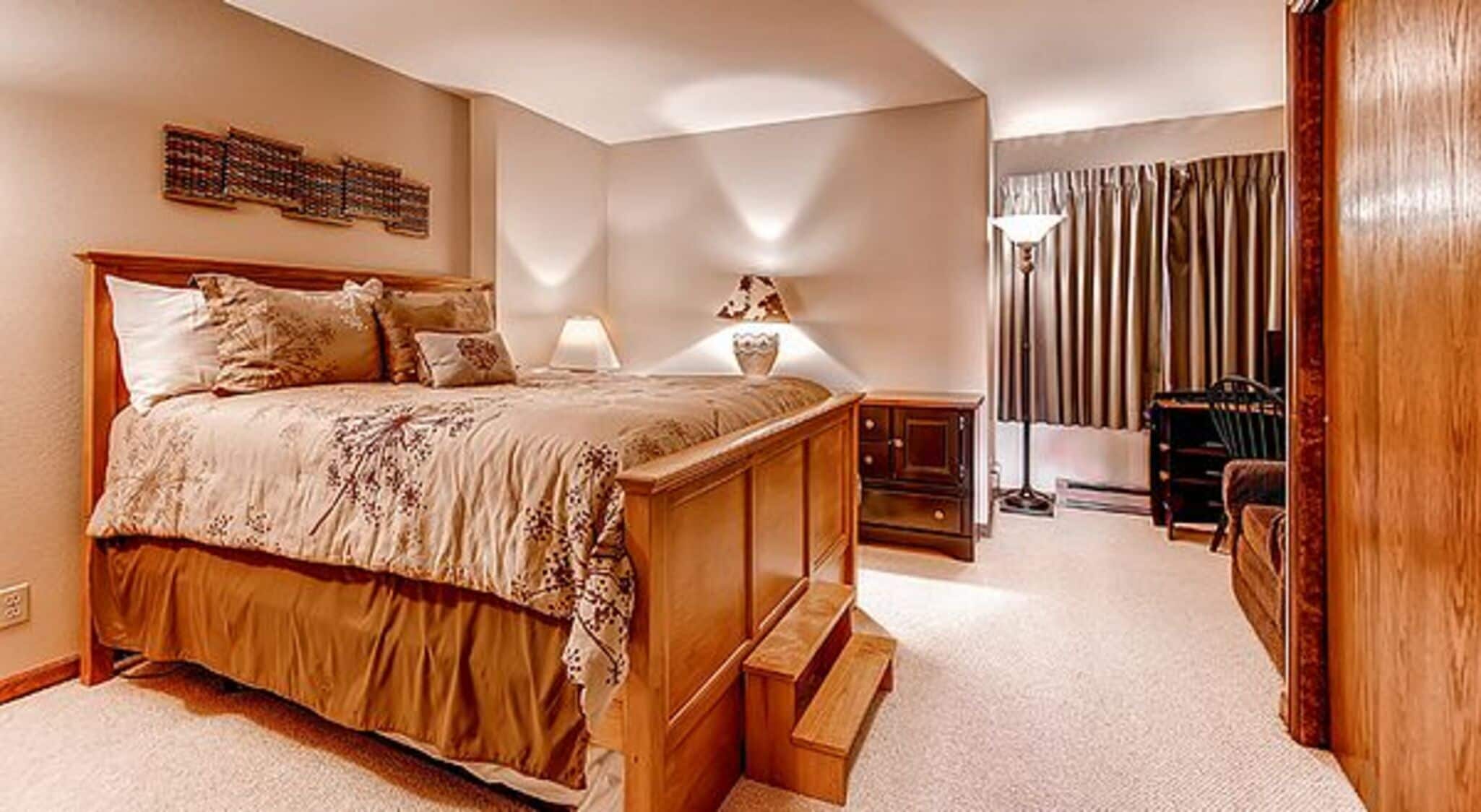 A bedroom with a large bed, bedside tables, a lamp, and a view of a room with curtains.