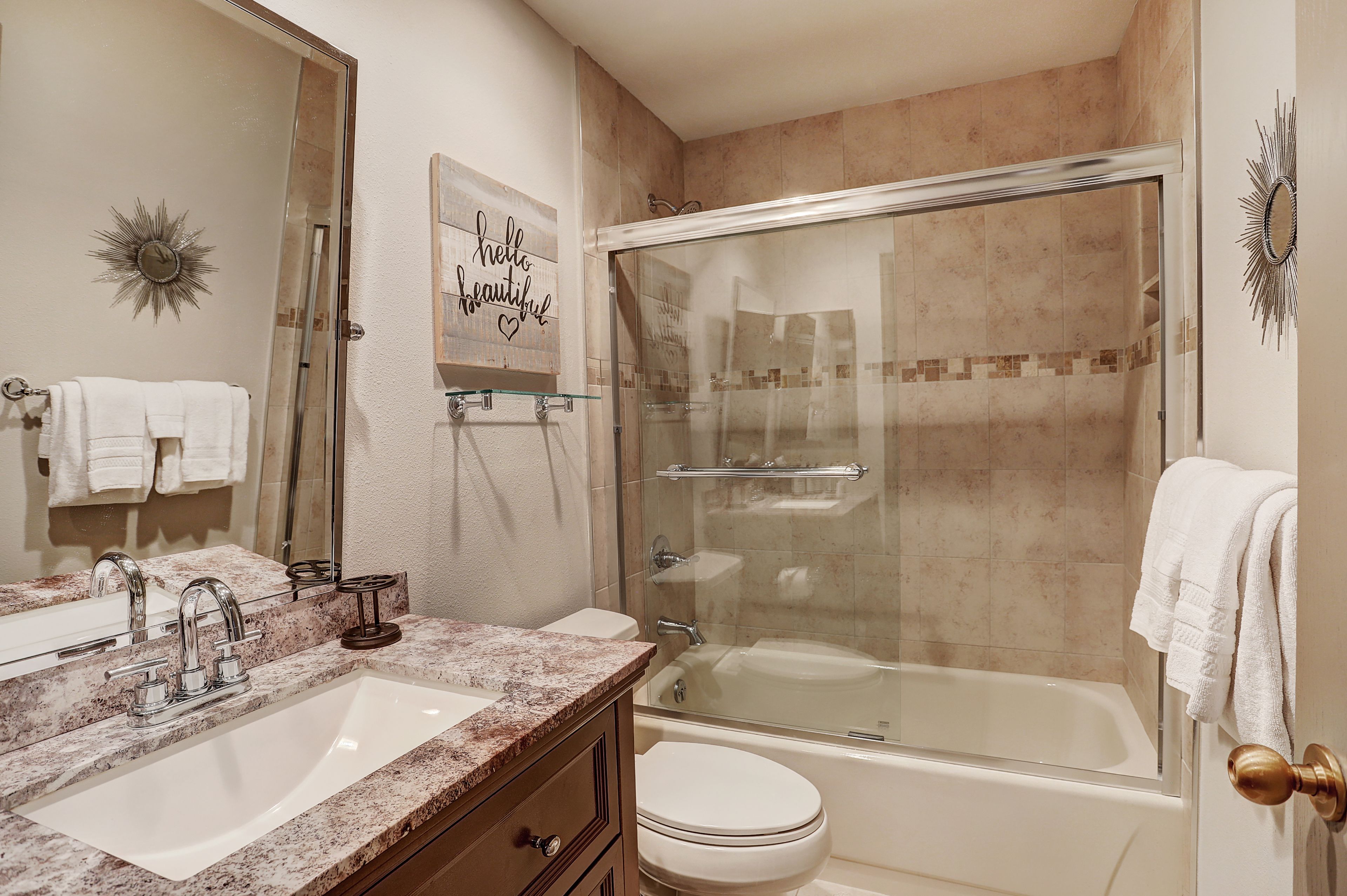 A bathroom with a glass-enclosed shower, a sink with a marble countertop, and a toilet.