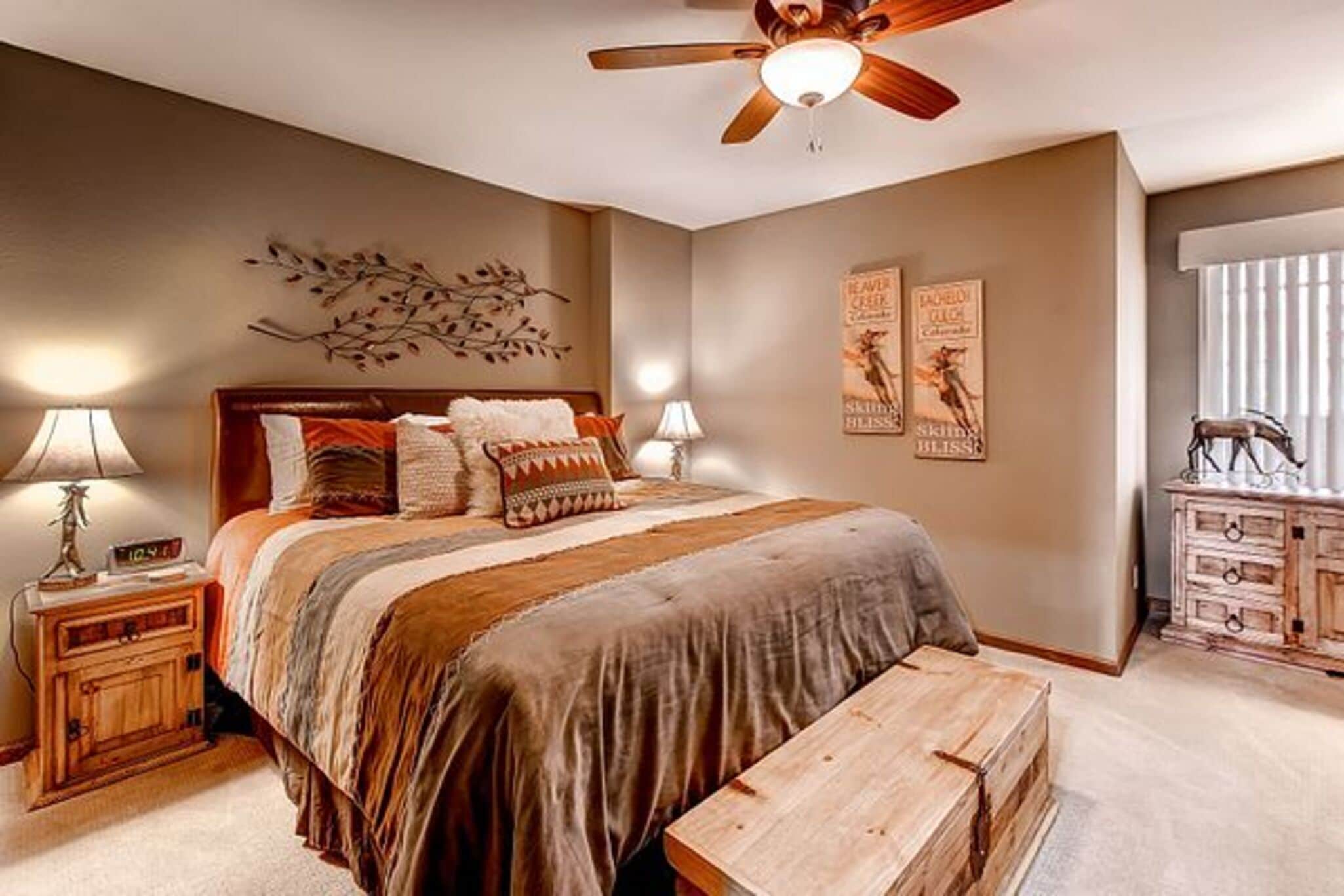 A bedroom with a bed, two bedside tables, a ceiling fan, wall art, and a dresser.