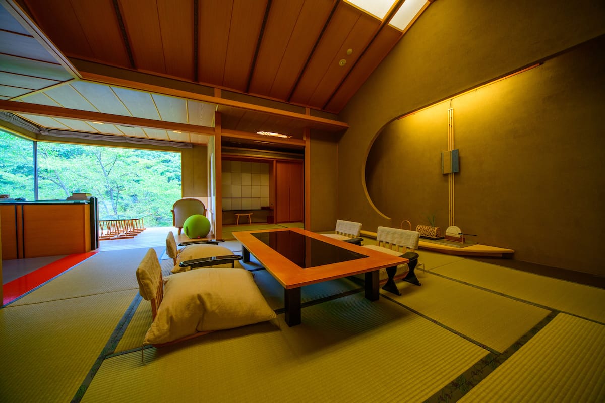 A tatami mat room with a low table, cushions, and a view of greenery outside.