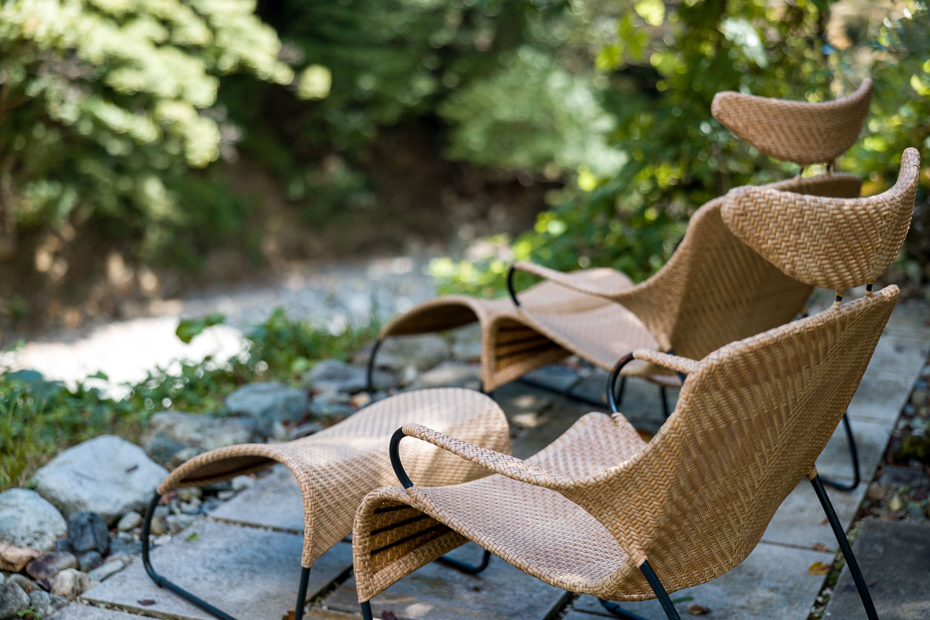 Wicker stoelen met metalen frames op een stenen pad.