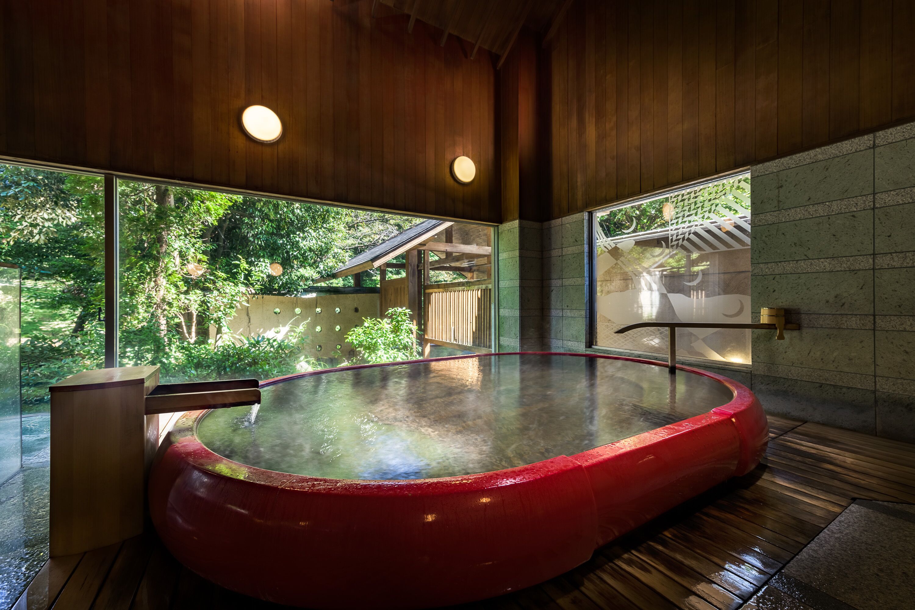 A hot tub in a wooden room with large windows and a view of greenery outside.