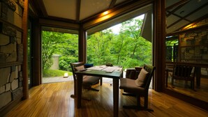 Comedor con mesa y sillas de madera, ventanas amplias con vistas a un jardín exuberante.