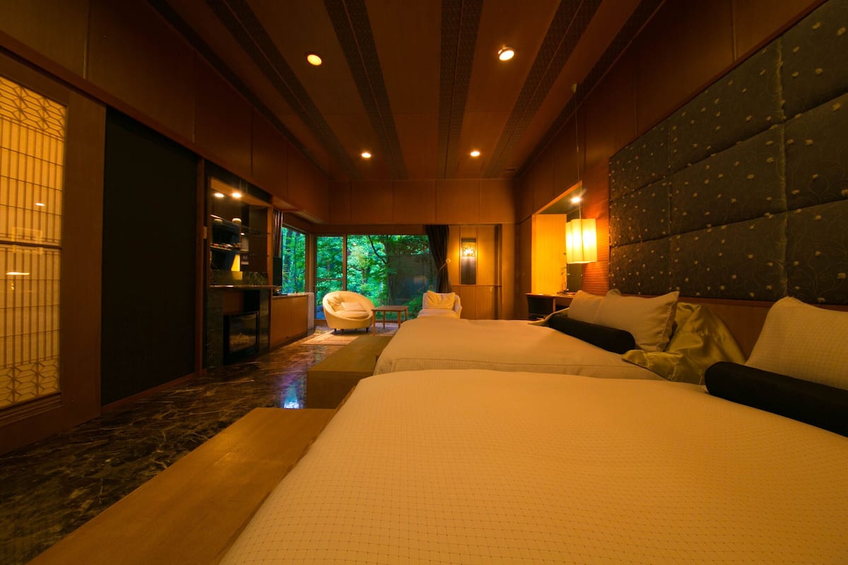 A hotel room with two beds, a seating area, and a view of greenery outside.
