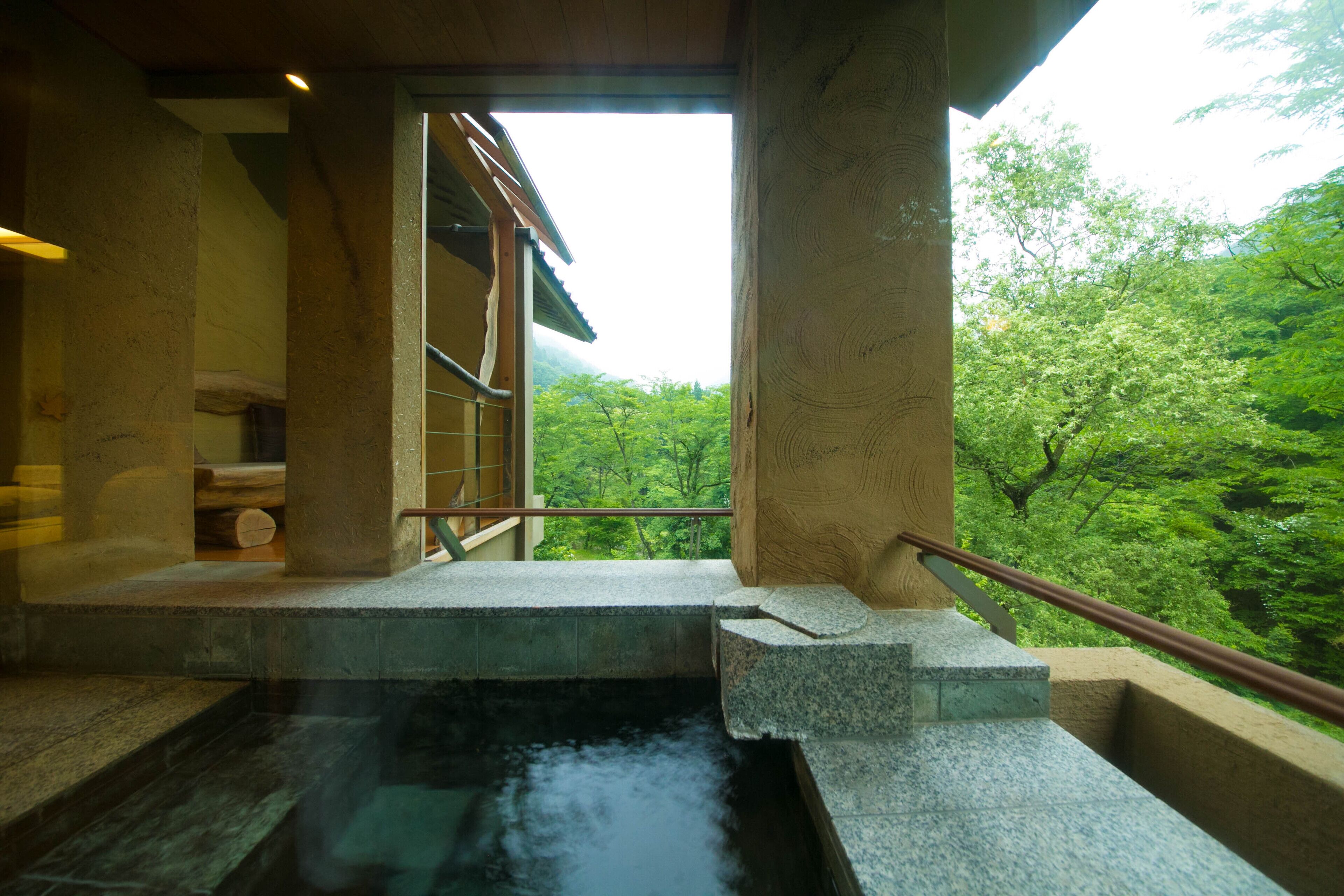A traditional Japanese onsen with a stone bath, wooden architecture, and a view of lush greenery.