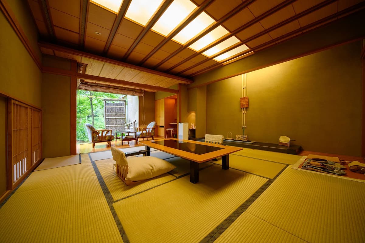 A traditional Japanese room with tatami flooring, a low table, and sliding doors leading to a garden.