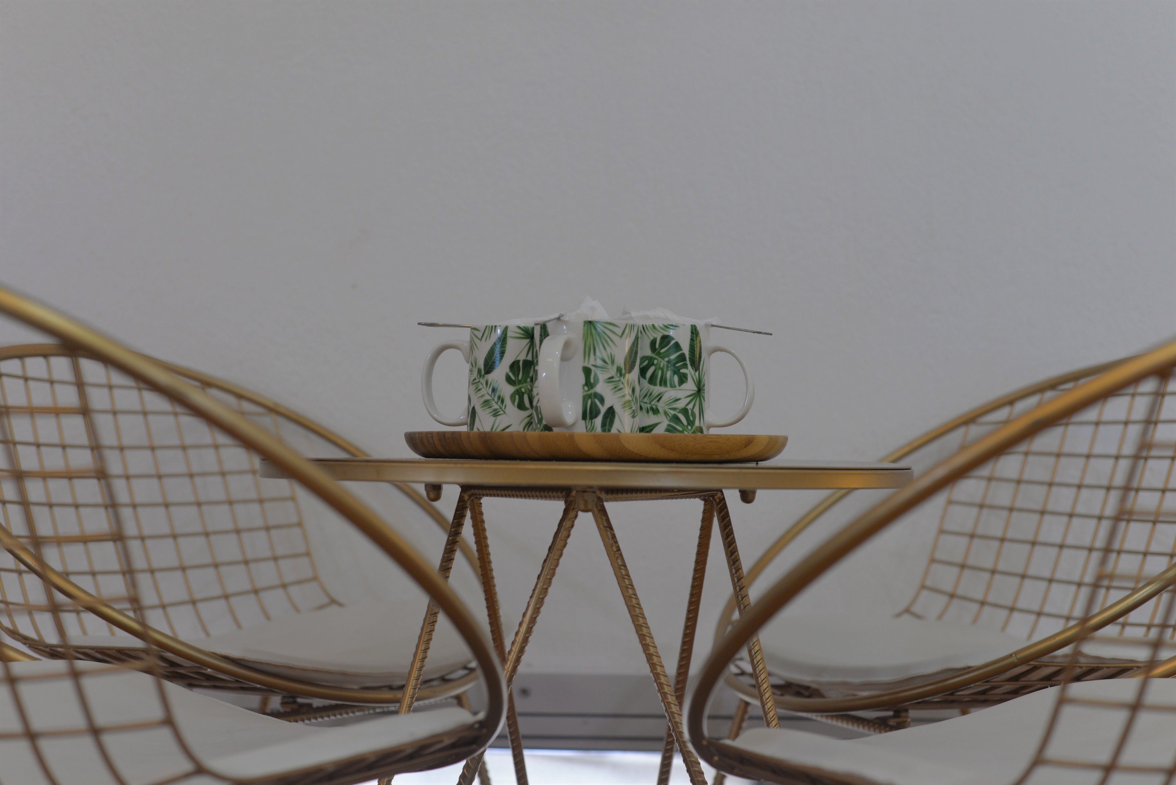 A table with a white mug and saucer, a wooden tray, and a wicker chair.