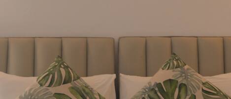 A bed with a headboard, two pillows with a leaf pattern, and a painting of a blue ocean above the bed.