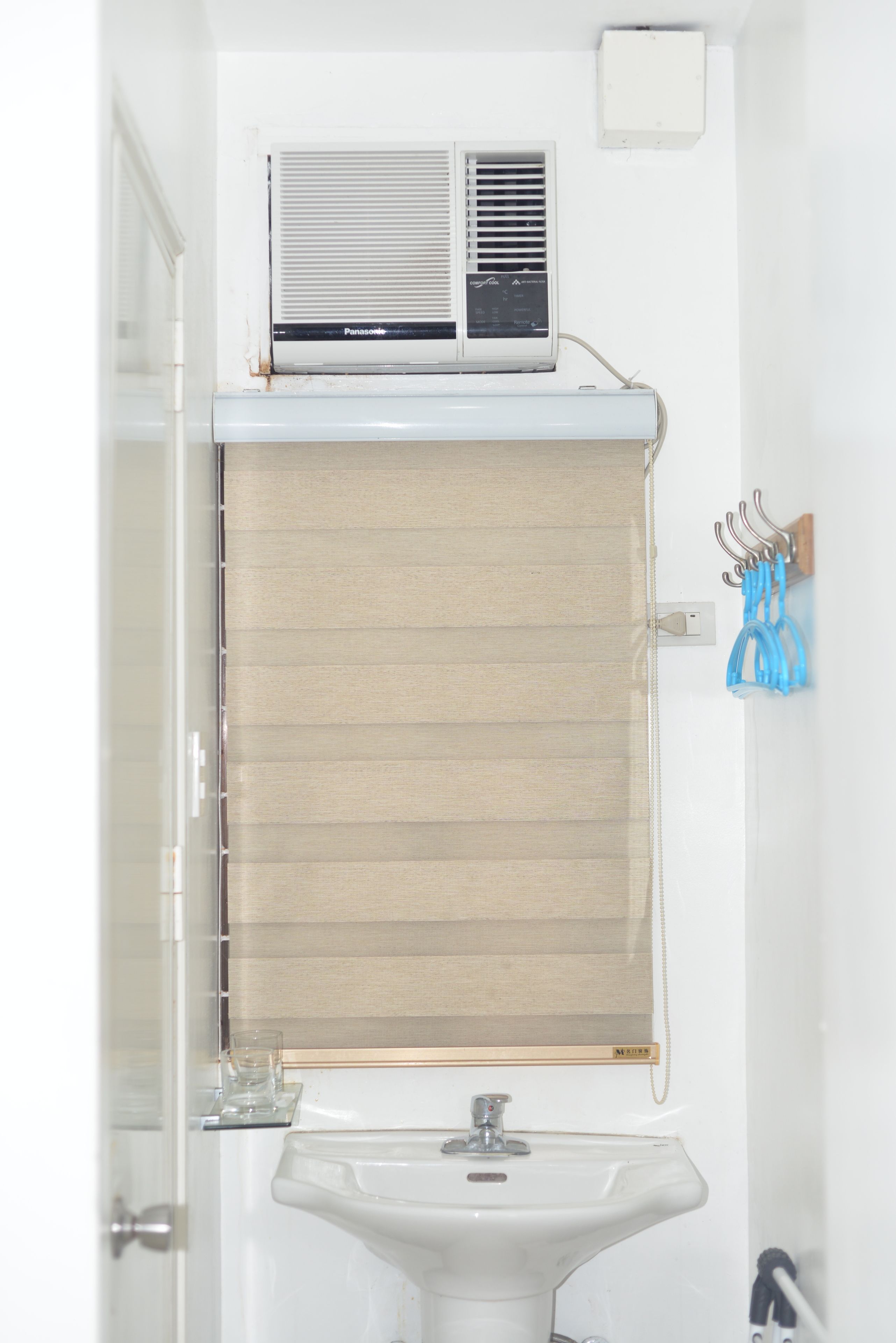 Un baño con un lavamanos blanco, un perchero con toallas azules y un aire acondicionado Panasonic montado sobre el lavamanos.