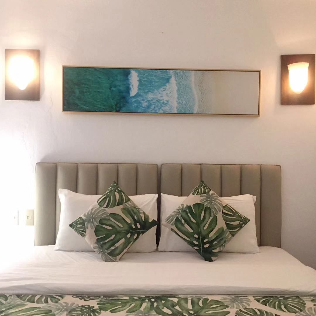 A bed with a headboard, two pillows with a leaf pattern, and a wall-mounted painting above.