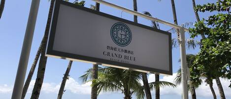 A sign for Grand Blue Beach Hotel with palm trees and boats in the background.