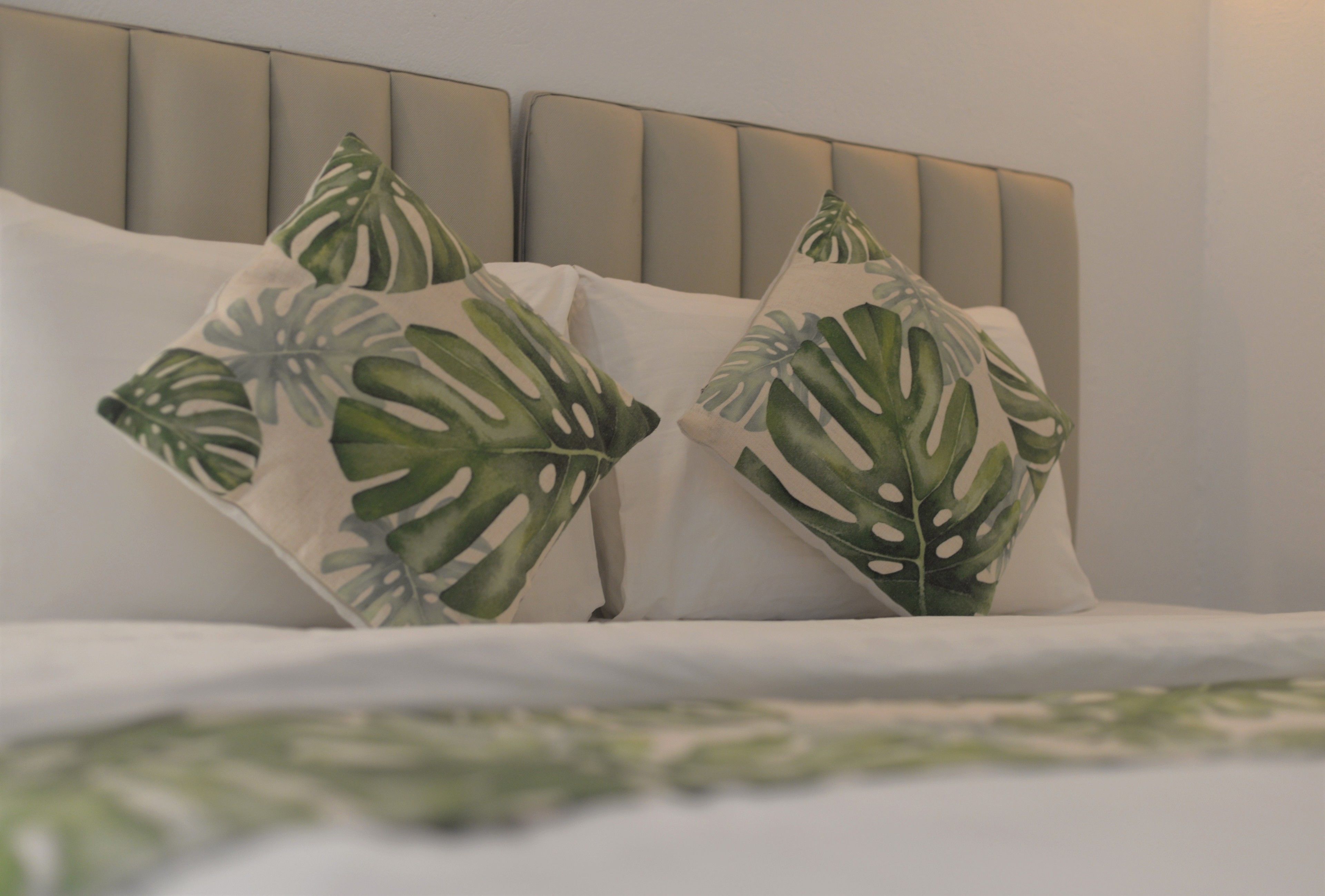 Un lit avec une literie blanche et deux coussins décoratifs ornés d’un motif de feuilles.