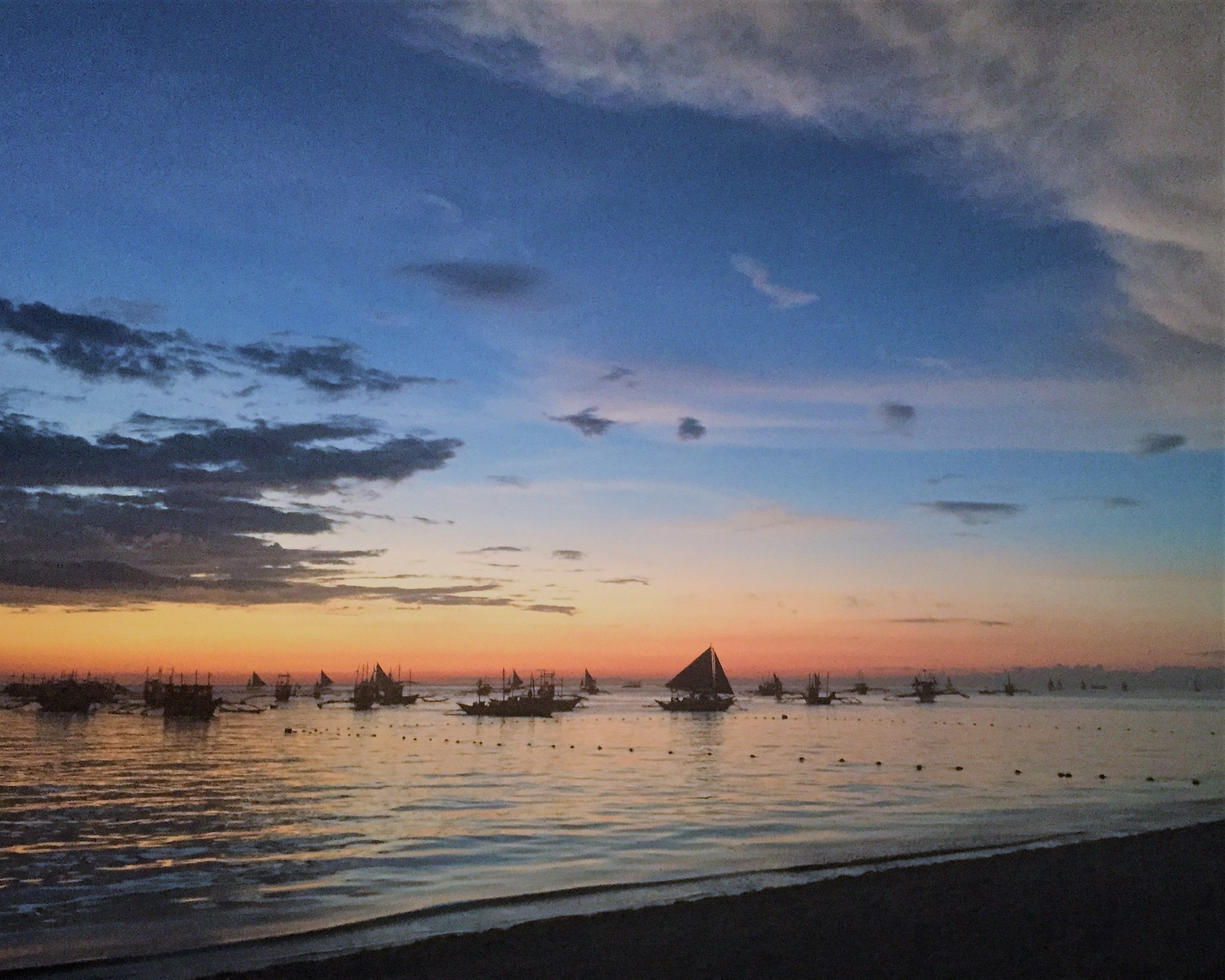 Mar tranquila al atardecer con varios barcos y una pequeña isla a lo lejos.
