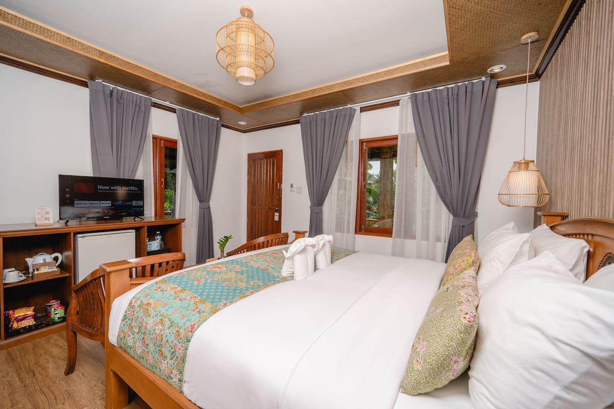 A hotel room with a bed, a desk with a television, a small refrigerator, and a window with curtains.