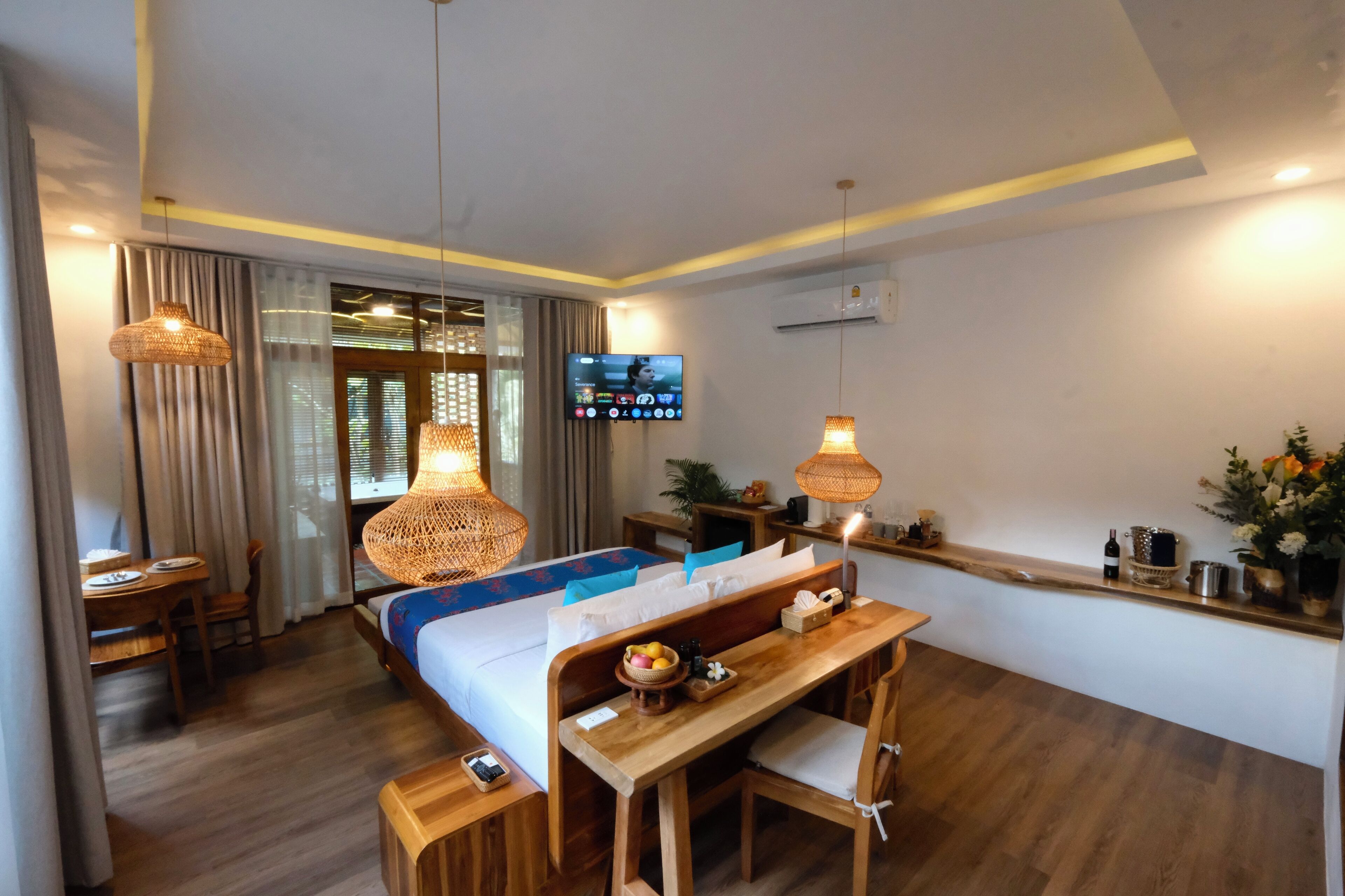 A hotel room with a bed, wooden desk, and chairs, a television, and a window with curtains.