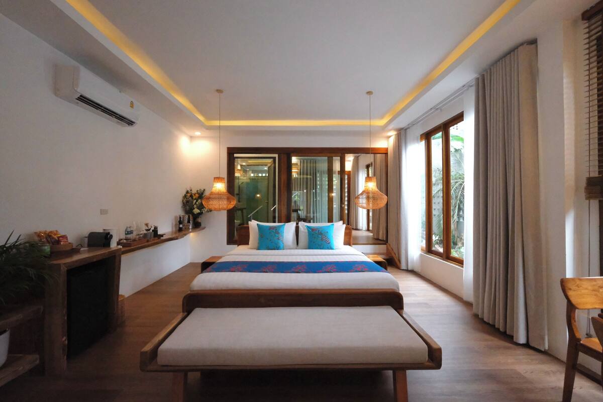Una habitación de hotel moderna con una cama grande, mesitas de noche, un escritorio y un amplio ventanal con cortinas.