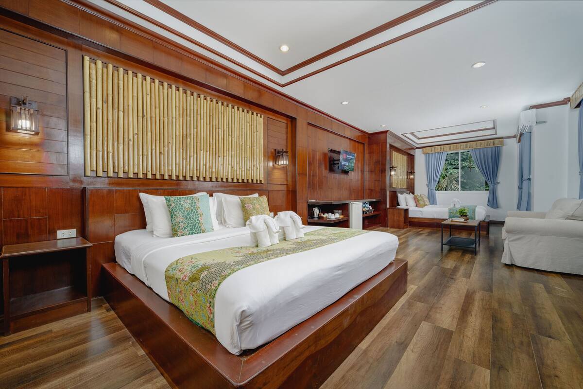A spacious hotel room with a large bed, wooden paneling, a television, and a seating area with a sofa and armchairs.
