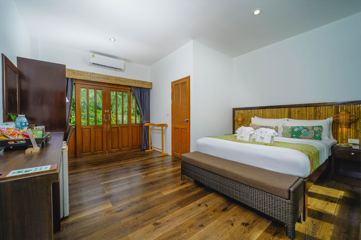 A hotel room with a wooden floor, a bed with a headboard, a desk with a chair, and a wardrobe.