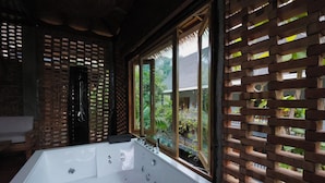 Un cuarto de spa con una bañera blanca grande, una ventana con celosía de madera y vistas a zonas verdes.