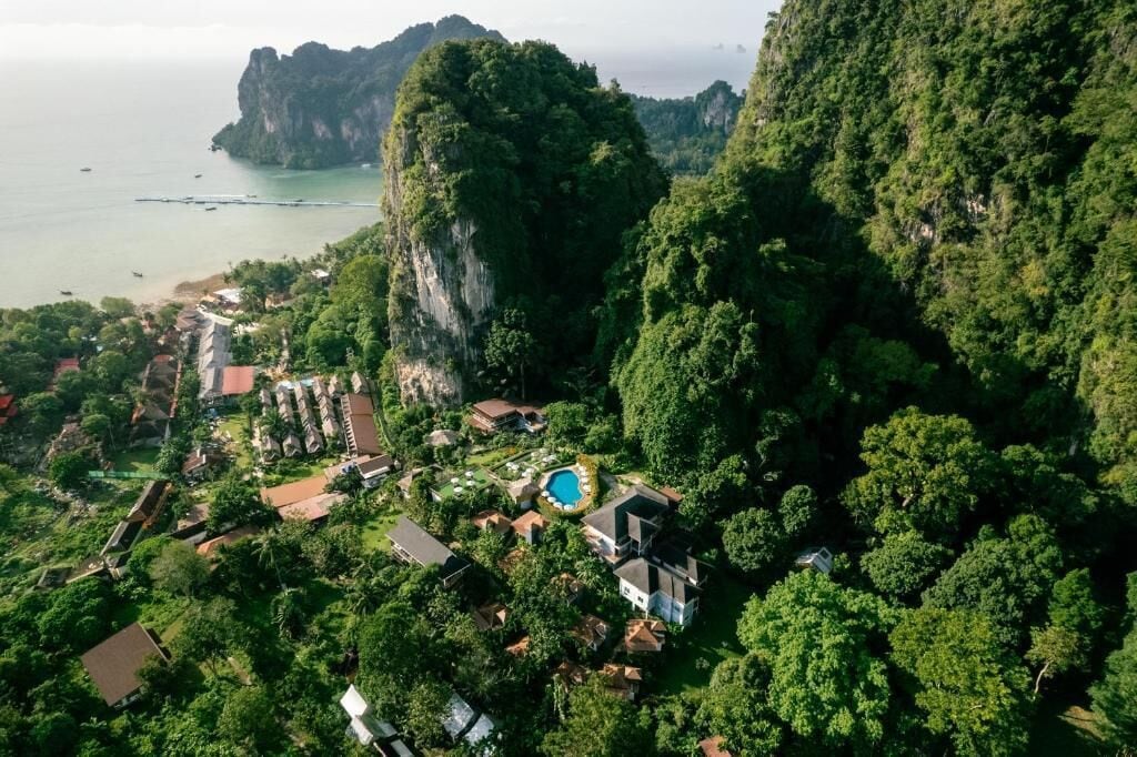 Luchtbeeld van een resort met een zwembad, omringd door weelderige begroeiing en een kustlandschap.