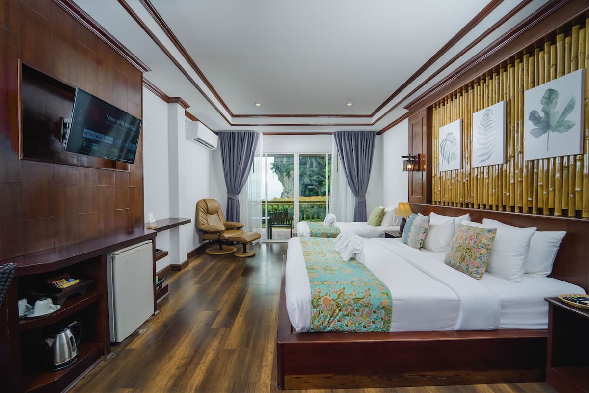 Una habitación de hotel con una cama grande, un televisor en la pared, una zona de estar con una silla y vistas al exterior.