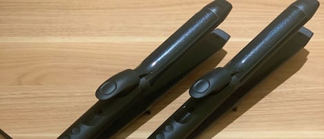 Deux fers à lisser les cheveux noirs, posés sur une surface en bois.
